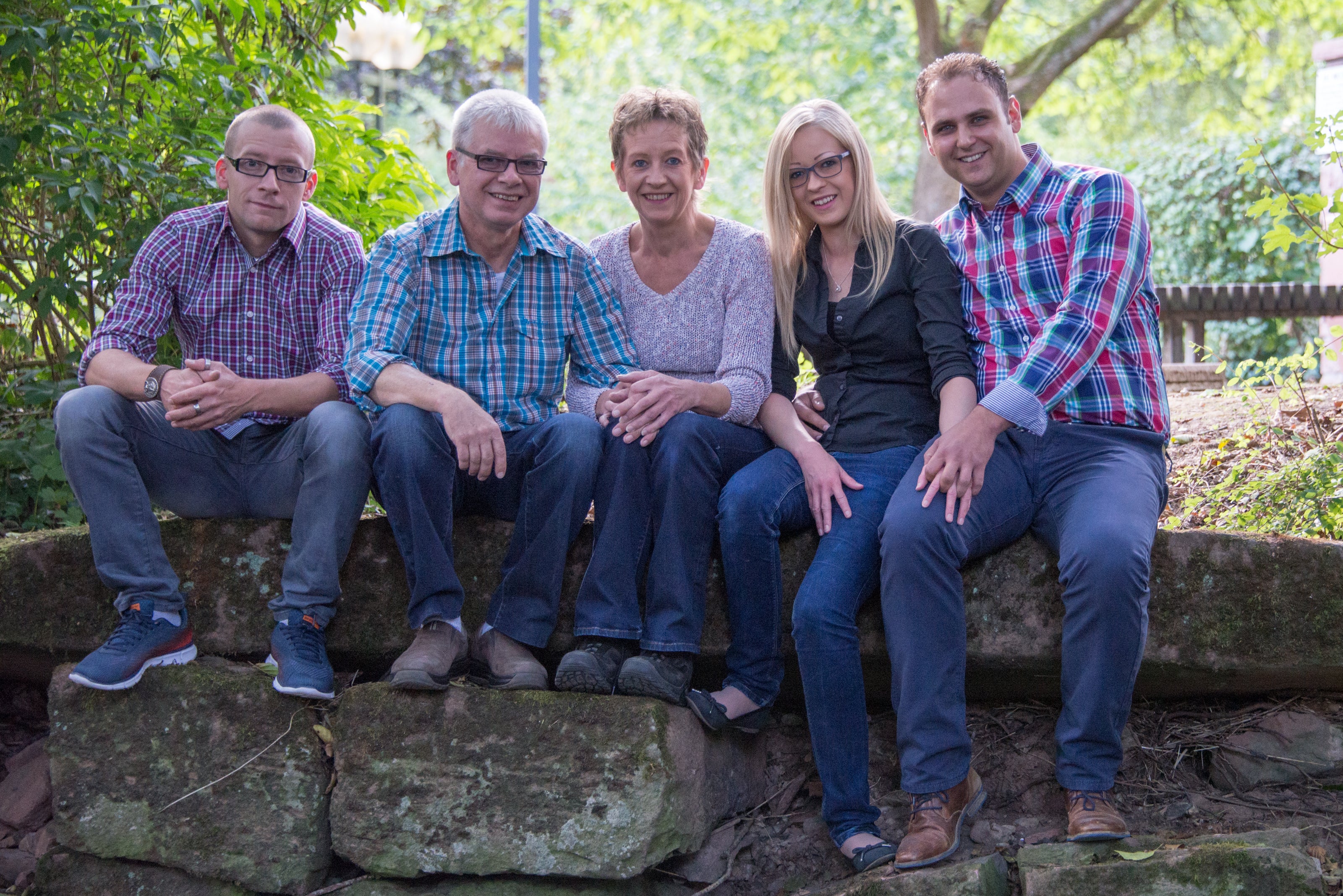 Ein Familienfoto auf dem zwei Frauen und drei Männer zu sehen sind die auf einem Stein direkt vor einem Bach Sitzen.