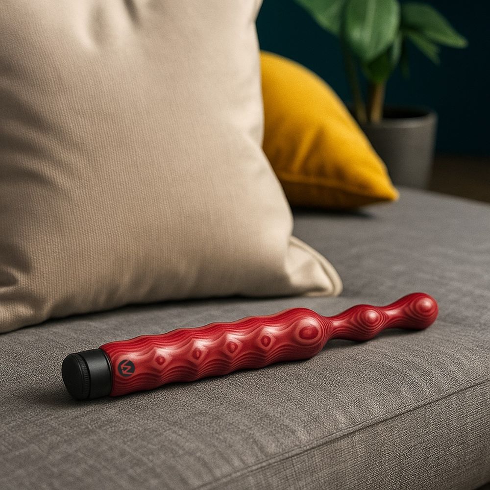 Auf einem Sofa liegt ein Holzvibrator Modell Doppelhummel in rot der Firma Waldmichlsholdi.